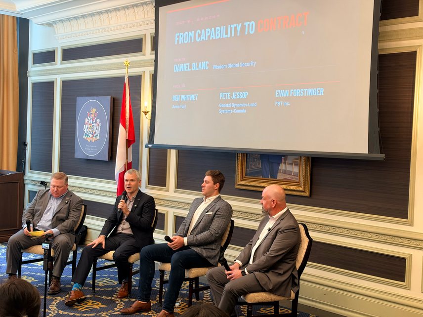 Four panellists seated on stage beneath a screen titled From Capability to Contract